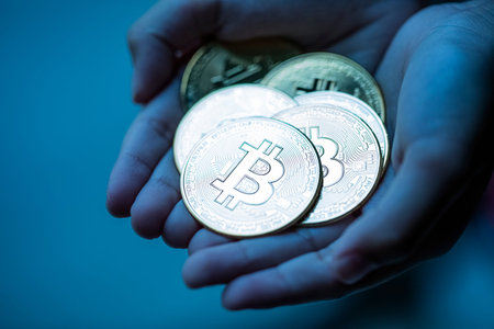 Shiny silver bitcoins in hand palm over dark blue background. Cryptocurrency market crash concept.