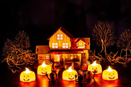 Creepy ghosts and pumpkins dancing on a yard in front of a lighted wooden house on a dark night. Halloween concept.の写真素材