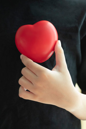 Young man holding a red heart or love on his chest with black shirt. Healthcare concept