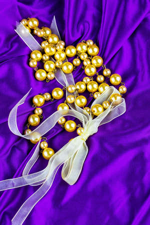 Golden pearls necklace with golden ribbon against shiny purple silkの写真素材