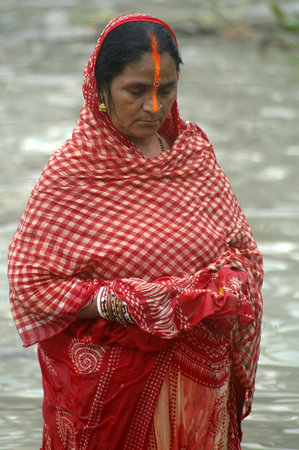 A woman is offering her prayer to sun god standing in the water of river Ganges during the Hindu...