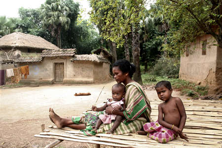 Indian tribal children are playing with their grandmother on a handmade bed in front of their house in tribal village near Durgapur, India.のeditorial素材