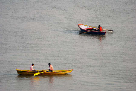 A couple of foreigner tourists enjoying morning boat ride on river Ganges at Varanasi, India. A number of migratory birds are floating and flying on river. Tourist used to feed them. A unique shop variety of items on boat runs by local people is also apprのeditorial素材