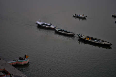 A group of people are enjoying the beauty of river Ganges by sitting on a ghat beside river in the afternoon while tourist boat is passing by at Varanasi, India.のeditorial素材