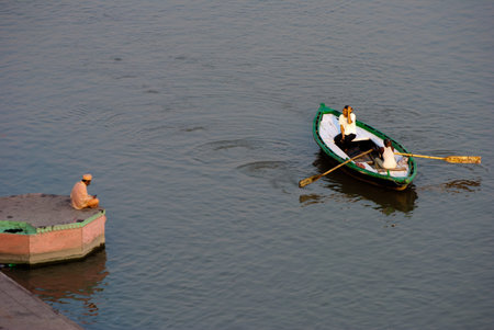 A holy man is enjoying the beauty of river Ganges by sitting on a ghat beside river in the afternoon while tourist boat is passing by at Varanasi, India.のeditorial素材