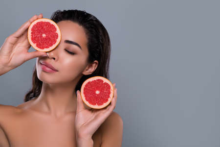 Photo of lovely lady holding half slice grapefruit enjoying hygiene balm on empty space on grey color backgroundの写真素材