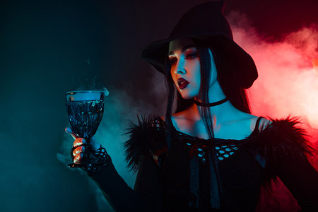 Photo of stunning evil witch lady prepare magical liquid dark potion in goblet over mist neon backgroundの写真素材