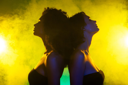 Photo of classy chic girls stand back to back couple dancing in night club over bright shine mist neon backgroundの写真素材