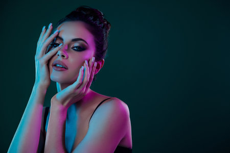 Portrait of young model girl with smokey eyes touch face at party for aristocrats isolated on green color backgroundの写真素材