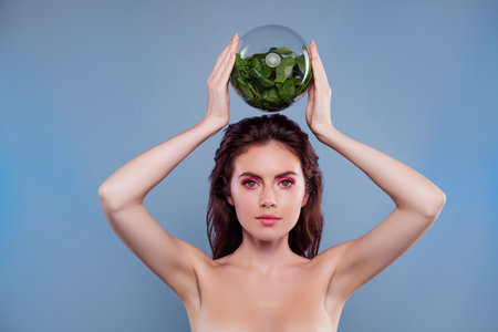 Photo of woman hold over head glass globe with plant organic ingredients isolated grey color backgroundの写真素材