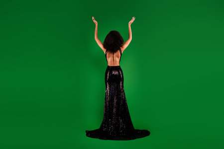 Rear view photo of glamour rich elegant lady posing with raised hands festive occasion over green color backgroundの写真素材