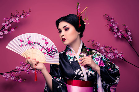 Photo of cute lovely elegant woman in kimono performing national dance isolated on pink color backgroundの写真素材
