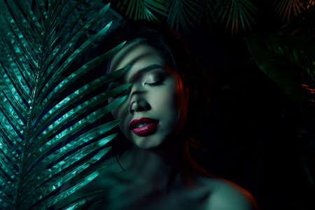Photo of vietnamese japanese girl on dark background closing eyes hide behind exotic palm treesの写真素材