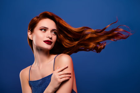 Photo of fashionable stunning lady advertising shampoo for long hair isolated on blue color backgroundの写真素材