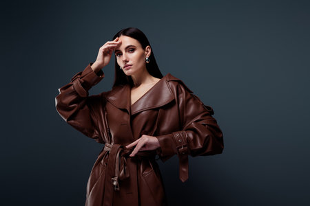 Fashionable stunning celebrity advertising stylish burgundy leather raincoat isolated on dark grey color backgroundの写真素材