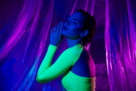 Photo of pretty model girl closed eyes hand touch chin green dress isolated on neon studio curtain backgroundの写真素材