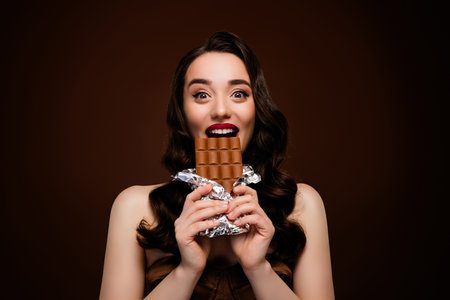 Photo of person eating a chocolate bar against brown backgroundの写真素材
