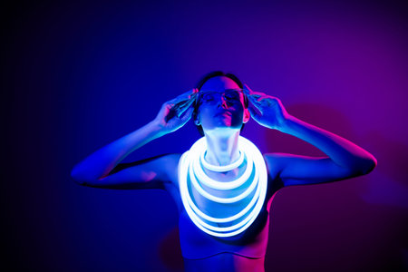 Contemporary young woman in dark blue neon glow, wearing futuristic fashion with style and...