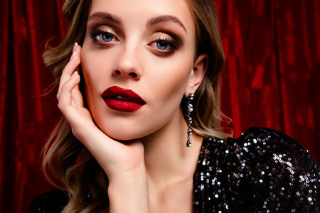 Pretty young woman in glamorous makeup with red velvet background, exuding beauty and...