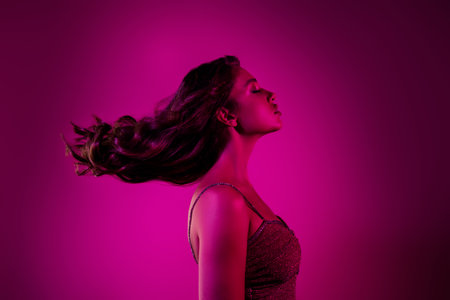 Elegant young woman with flowing hair against a vibrant pink backgroundの写真素材