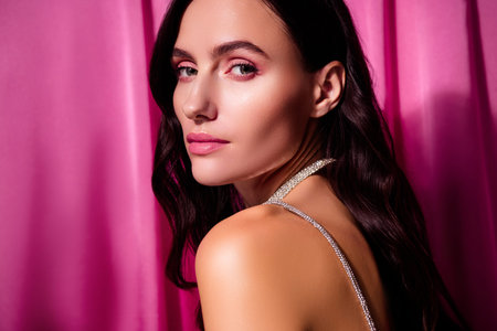 Glamorous woman with elegant hairstyle posing against a pink background in studioの写真素材