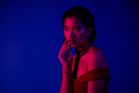 Photo of charming woman dressed top looking empty space touching chin isolated blue color backgroundの写真素材