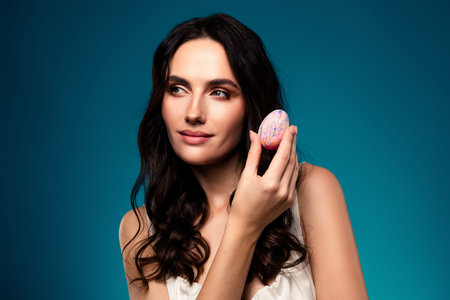 Glamorous Young Woman Holding a Decorated Easter Egg and Posing Against a Blue Gradient Backgroundの写真素材