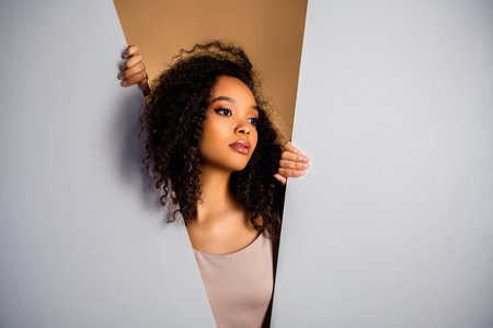 Stylish young woman posing with confidence through a creative cutout composition against a minimalist background.の写真素材