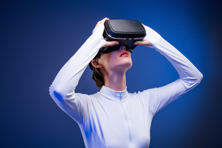 Young woman in white bodysuit exploring virtual reality with headset against illuminated blue backgroundの写真素材