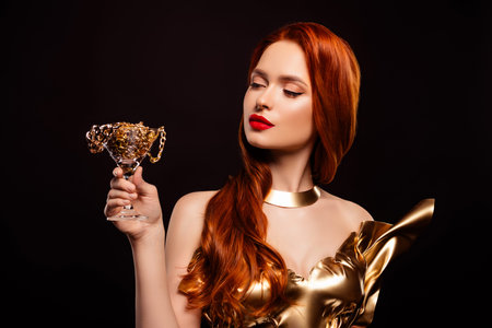 Successful red haired woman in a golden dress holding a glass with chains, conveying luxury and beautyの写真素材