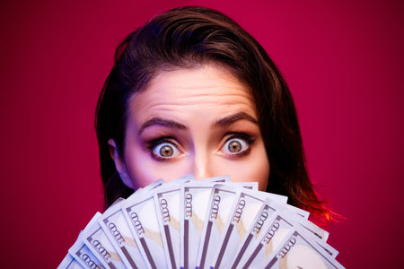 Excited Young Female Holding Cash in a Dramatic Pink Background Setting Depicting Wealth and Fortuneの写真素材