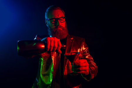 Elegant gentleman in neon light pouring drink, celebrating in glamorous suit in dark club settingの写真素材