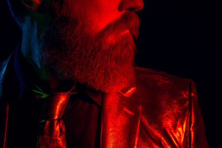 Charismatic mature man in glowing suit illuminated by vibrant red and blue neon lights against a dark backgroundの写真素材
