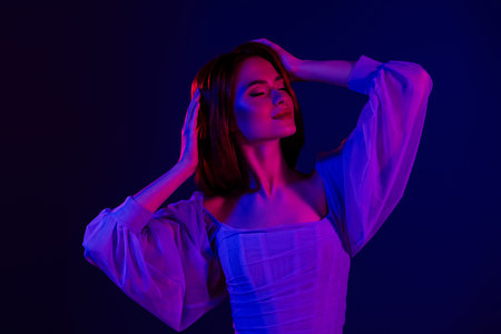 Portrait of a gentle woman with red hair in vibrant lighting against a blue background showcasing...