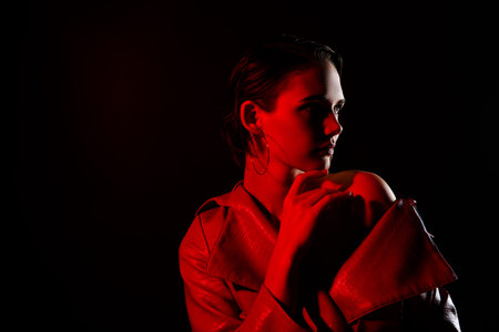 Photo of young female touch soft skin look empty space neon red light dressed jacket on black color...