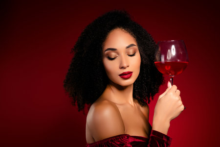 Chic attractive pretty lady with closed eyes celebrate holiday toast with wine glass on red backgroundの写真素材
