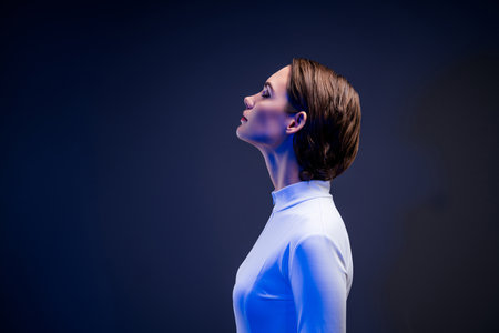 Side profile of a young woman with sleek brunette hair under blue neon lighting, expression serene, embodying beautyの写真素材