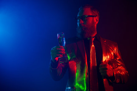Charismatic man in a glamorous suit holding a drink under neon lights at a partyの写真素材
