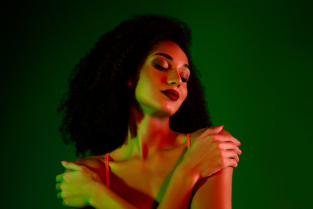 Graceful young woman with curly hair in artistic lighting, exuding confidence and eleganceの写真素材