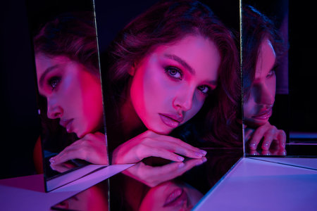 Portrait of a woman reflecting on mirrors under stylized pink and blue neon light showcasing fashion...