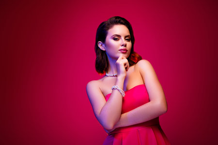 Attractive young woman in a stylish pink dress poses confidently on a vibrant gradient backgroundの写真素材