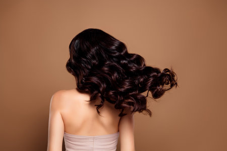 Elegant brunette woman with wavy hair showcasing style and beauty on beige background, embodying glamourの写真素材