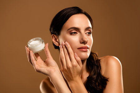 Beautiful woman with radiant skin applying cream for skincare on beige backgroundの写真素材