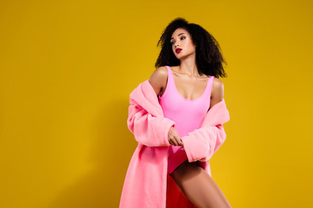 Fashionable woman wearing pink bodysuit on vibrant yellow background, styled with elegance and confidenceの写真素材