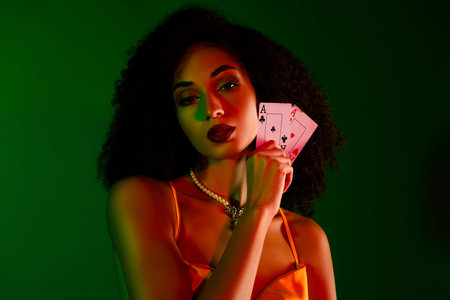 Young elegant woman with a stylish cocktail dress and playing cards, posing against a green gradient backgroundの写真素材
