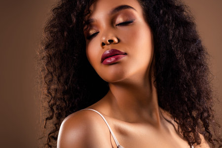 Portrait of a young woman with flawless skin and curly hair posing elegantly against a soft brown backgroundの写真素材