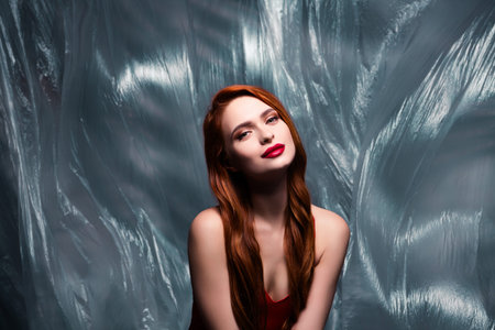 Lovely Woman with Red Hair Posing Elegantly in Studio Setting with Stylish Plastic Cellophane Backgroundの写真素材