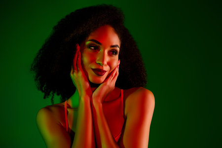 Elegant young woman with glowing skin in stylish attire against a green background, showcasing beauty and glamourの写真素材