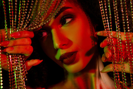 Beautiful young woman with glowing skin poses under festive lighting effects and shimmering decorationsの写真素材