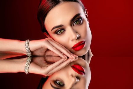 Elegant young woman with glamorous red makeup posing against a vibrant red background in a luxurious jewelry styleの写真素材